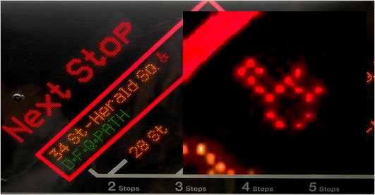 an LED screen for a subway car showing next stops. A wheelchair symbol made of 16 red LEDs is magnified.